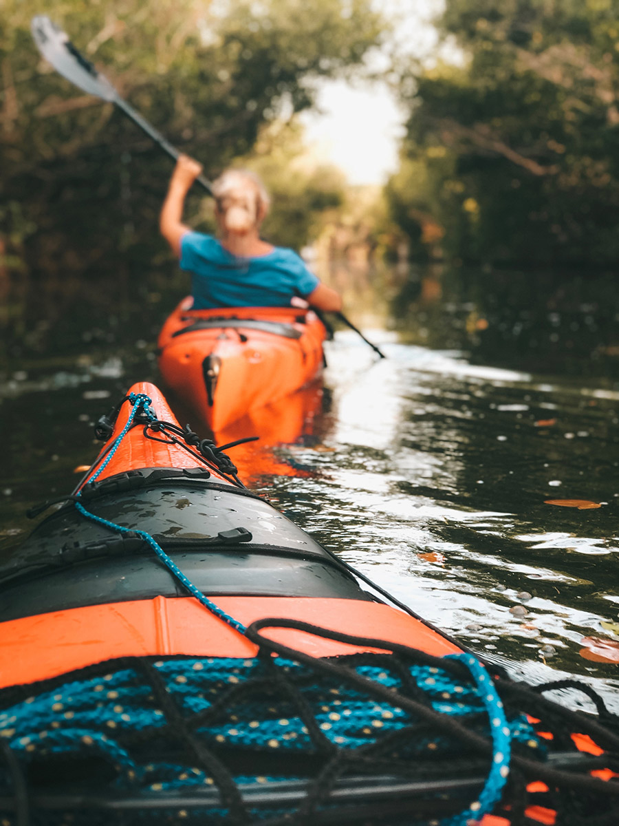 A woman paddling an orange kayak with the tip of another kayak behind her.